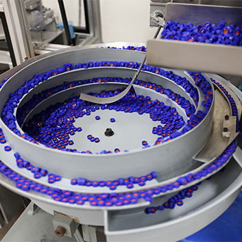 Industrial equipment for a silicone rubber seal manufacturer. Hundreds of small purple seals swirl around in a cylindrical machine.