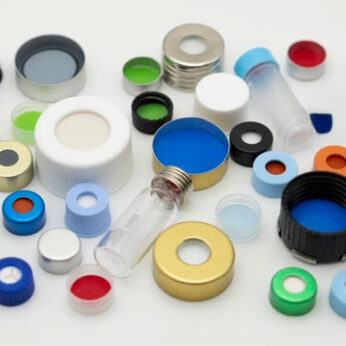 Assorted colorful laboratory vial caps, liners, and glass vials scattered on a white surface