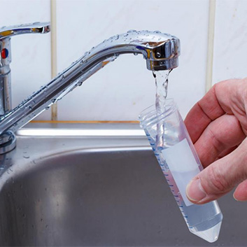 A water faucet with a hand holding a test tube for drinking water analysis