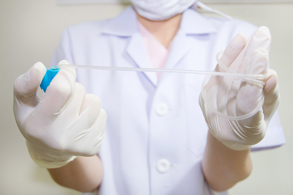 A medical professional in white gloves and a lab coat holding clear medical tubing