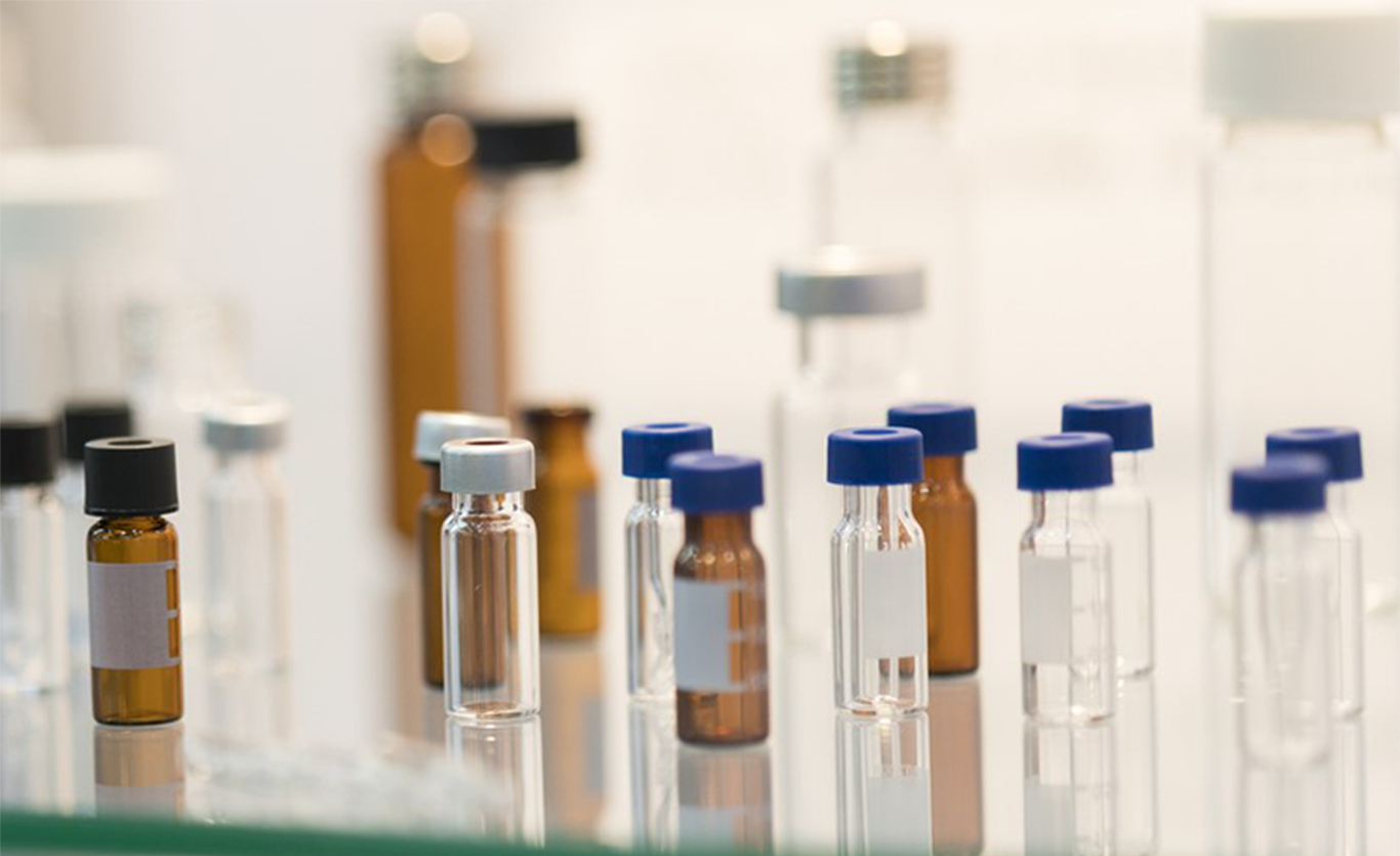 Scientist pouring liquid into a flask during beverage testing with lab equipment in the background
