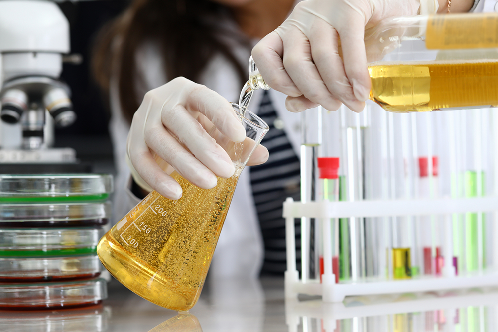 Scientist pouring liquid into a flask during beverage testing with lab equipment in the background