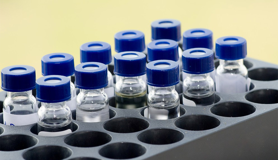 A rectangular laboratory tray organized with multiple clear glass sample vials featuring blue caps