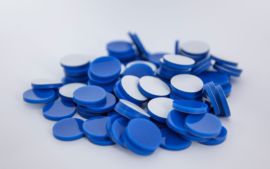 A pile of round blue cap liners with white backing for laboratory vials