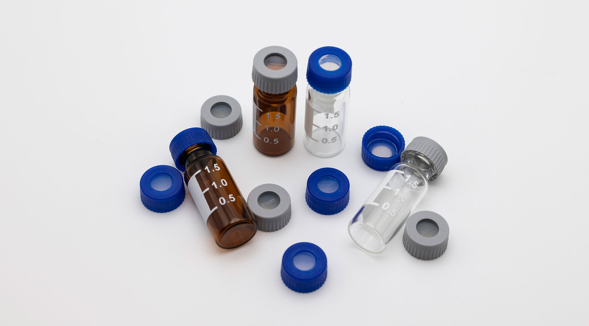 Clear and amber graduated glass sample vials scattered with blue and grey screw